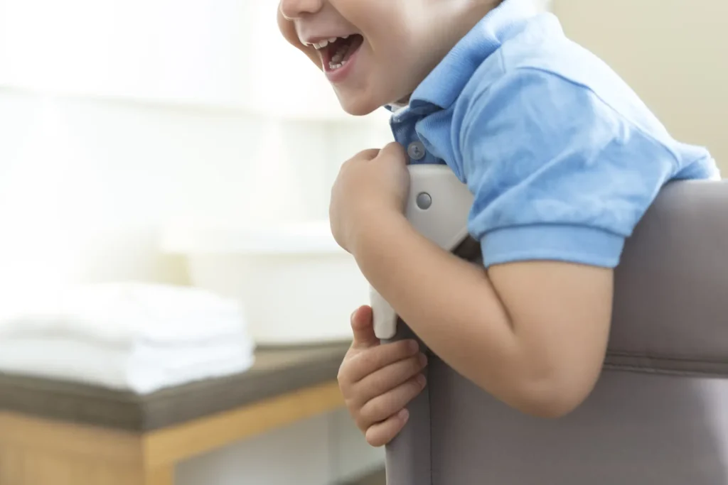 Nell'immagine c'è un bambino che abbraccia l'angolo di una sedia. Lui indossa una polo azzurra e sorride