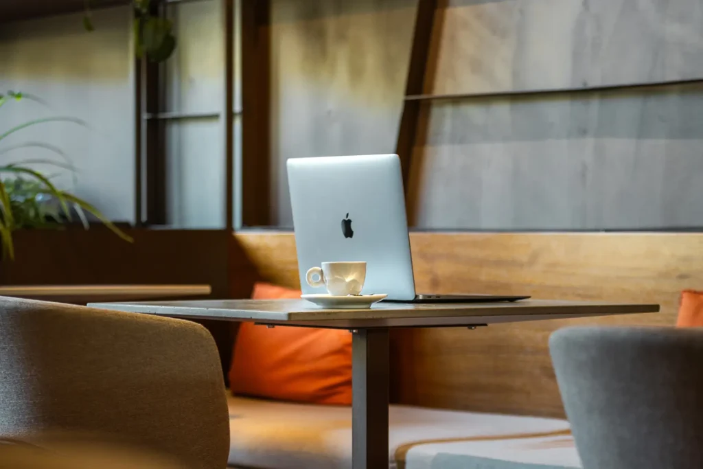 Nell'immagine c'è lo spazio coworking dell'hotel con un tavolino e sedie. Sul tavolino c'è una tazzina e un laptop aperto