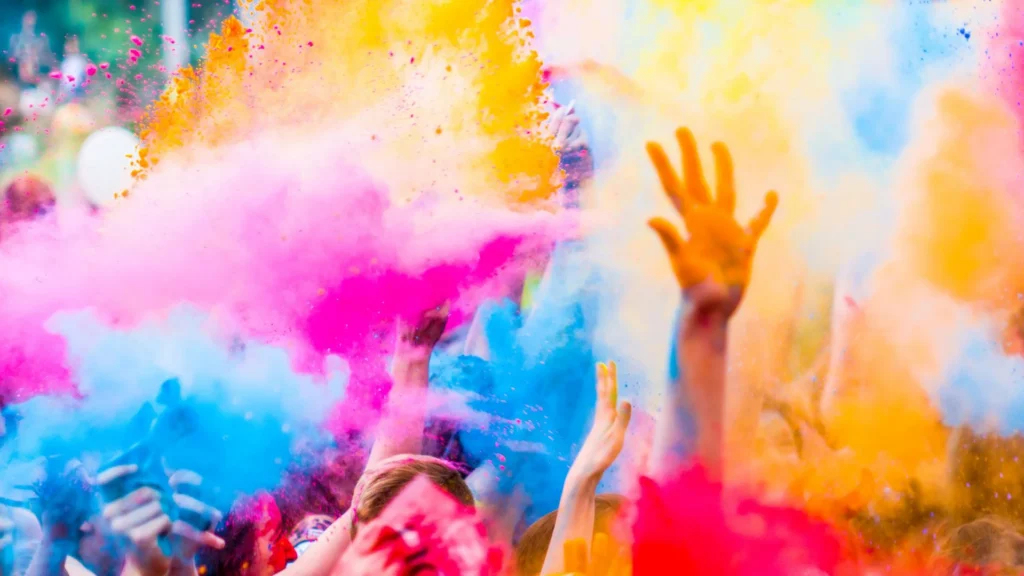 Delle persone festeggiano con le braccia rivolte verso il cielo lanciando in aria della polvere colorata